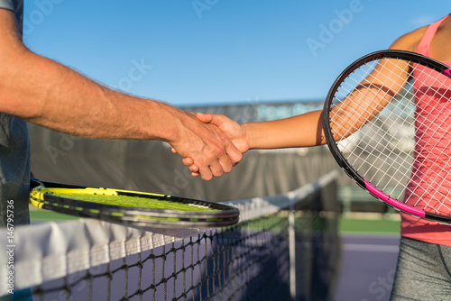 Tennis players shaking hands at court net at end of fun game. Man and woman playing recreational tennis handshaking with tennis racquets.