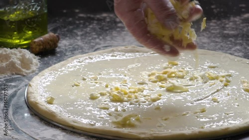 Cooking pizza. Hands adding fresh grated cheese to pizza dough. Pizza ingredients on the floured wooden table. Slow motion. photo