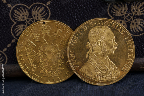 Close-up view of two on one another Austria-Hungary thalers, avers and revers of golden coin-ducats from 1915 with Kaiser Franz Joseph I, leaning on treasure chest and dark environment