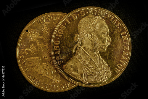 Close-up view of two on one another Austria-Hungary thalers, avers and revers of golden coin-ducats from 1915 with Kaiser Franz Joseph I, on dark background photo