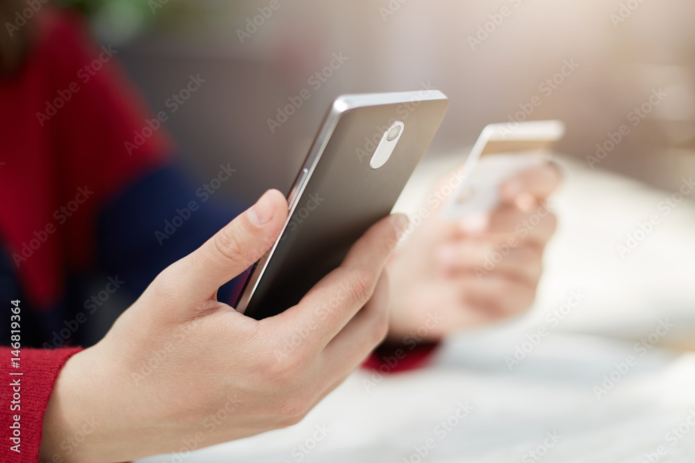 A close-up of female`s hands holding smartphone and credit card paying bill online via internet, making transaction, using mobile bank application on cell phone. Modern technology and online payment. A close-up of female`s hands holding smartphone and credit card paying bill online via internet, making transaction, using mobile bank application on cell phone. Modern technology and online payment.