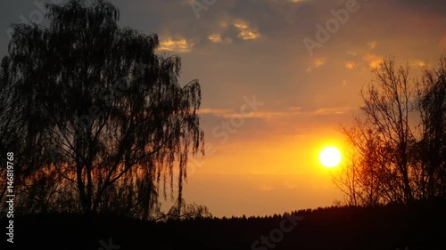 Spring sunset timelaps with dramatic clouds, orange colors and tree silhouette. photo