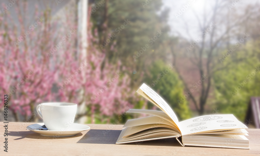 Coffee cup with open book over spring garden Coffee cup with open book over spring garden