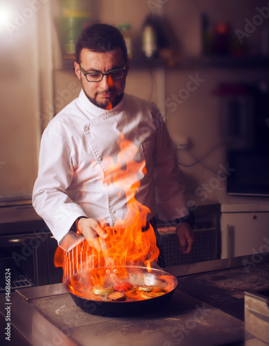 The chef prepares the dish on the stove with an open fire in the kitchen of the restaurant.