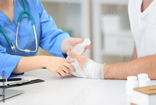 Orthopedist applying bandage onto patient's hand in clinic, closeup