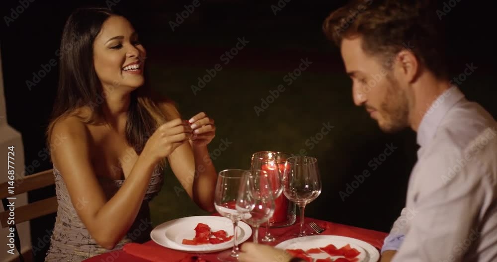Good looking man makes joke and gestures at beautiful dinner date across red covered table Good looking man makes joke and gestures at beautiful dinner date across red covered table