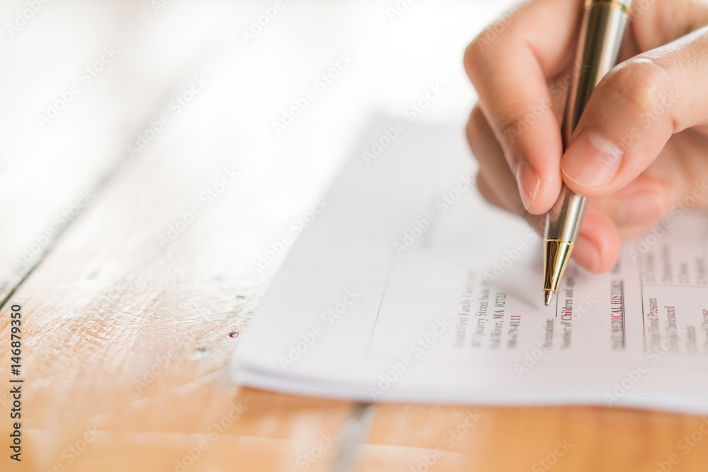 Hand with pen over application form . Hand with pen over application form .