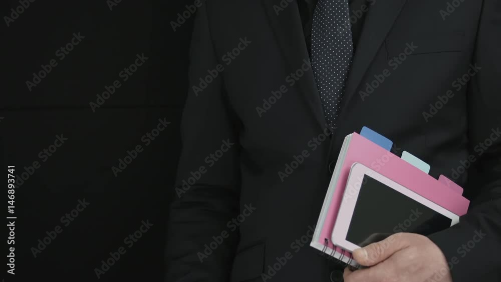 Businessman In Suit And A Blue Tie Holding Documents And A Tablet And Explaining A Business Matter Using A Pen Businessman In Suit And A Blue Tie Holding Documents And A Tablet And Explaining A Business Matter Using A Pen