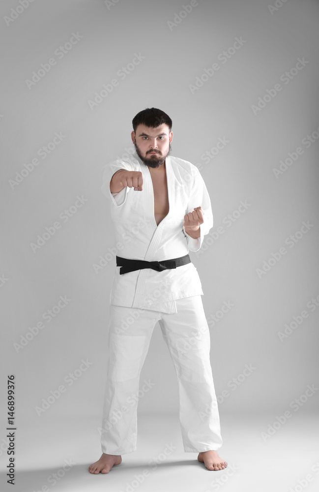 Young sporty man in kimono on light background