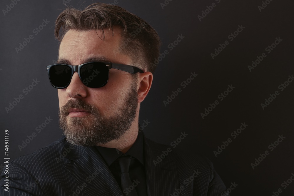 A brutal man with a beard and a stylish hairdo in a black suit and sunglasses A brutal man with a beard and a stylish hairdo in a black suit and sunglasses