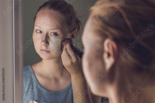 Spa Woman applying Facial green clay Mask. Beauty Treatments. Close-up portrait of beautiful girl applying facial mask photo