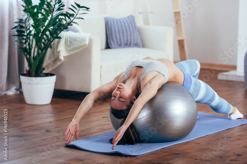 Young sportswoman doing exercises with ball on a mat at home