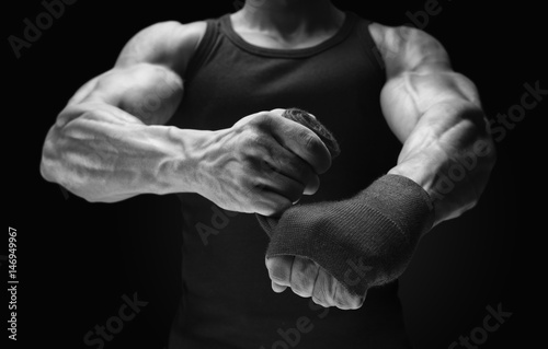 Close-up photo of strong man wrap hands on black background Man is wrapping hands with boxing wraps Strong hands and fist, ready for training and active exercise