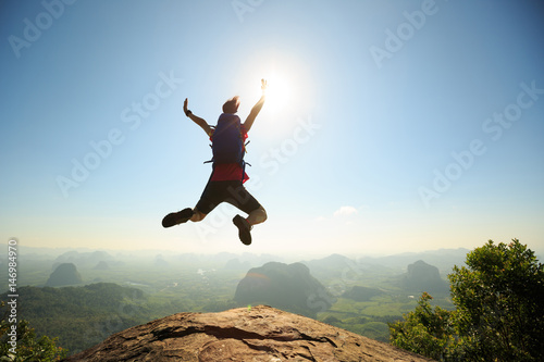 cheering successful young woman hiker jumping on mountain peak