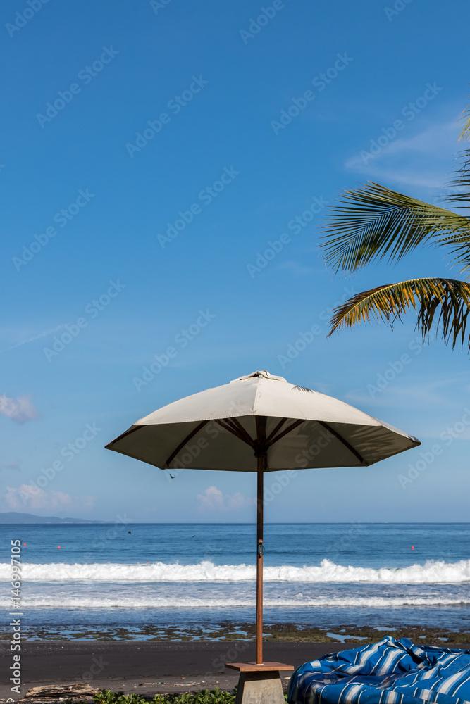 Beach umbrella on a sunny day, sea in background. Tropical beach with black sand. Beautiful sky. Paradise island Bali, Indonesia.