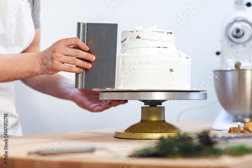 Man's hand levels cream on cake, cake decor on white background, close-up