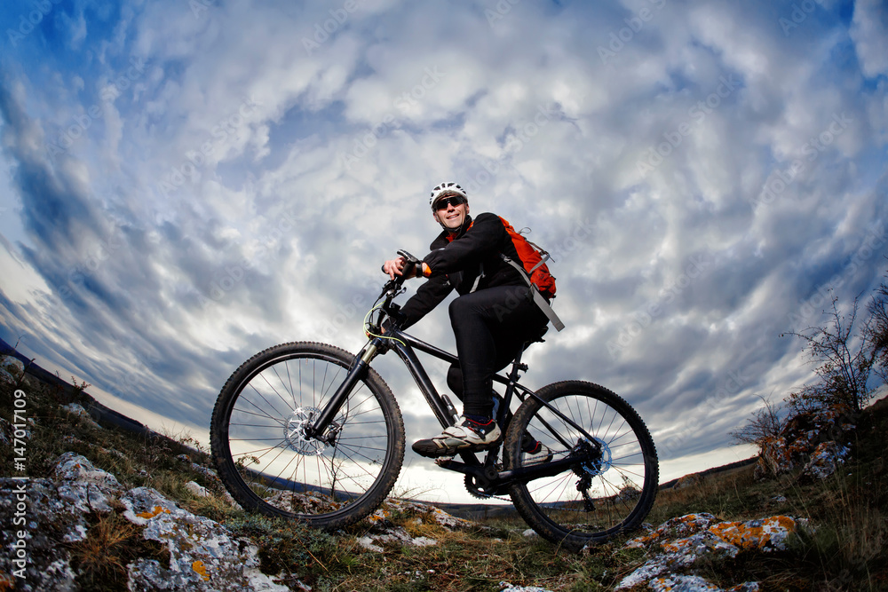 Portrait of the mountain cyclist standing with bike on the rocky hill against dramatic sky with clouds. Portrait of the mountain cyclist standing with bike on the rocky hill against dramatic sky with clouds.