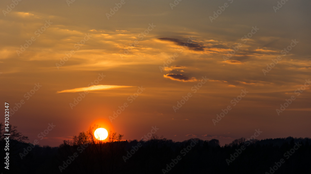 Red sky with few clouds during sunset over the hill. Silhouette of meadow. Strong sun is near above the horizon. Red sky with few clouds during sunset over the hill. Silhouette of meadow. Strong sun is near above the horizon.