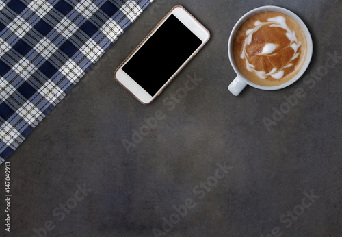 Cell phone and hot cappuccino with fabric on dark gray wooden table, top view background