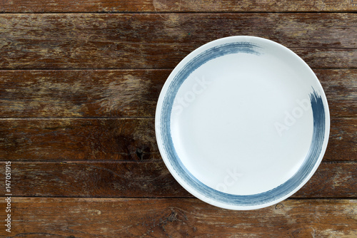 Top view of white empty ceramic plate on wooden background with copy space.