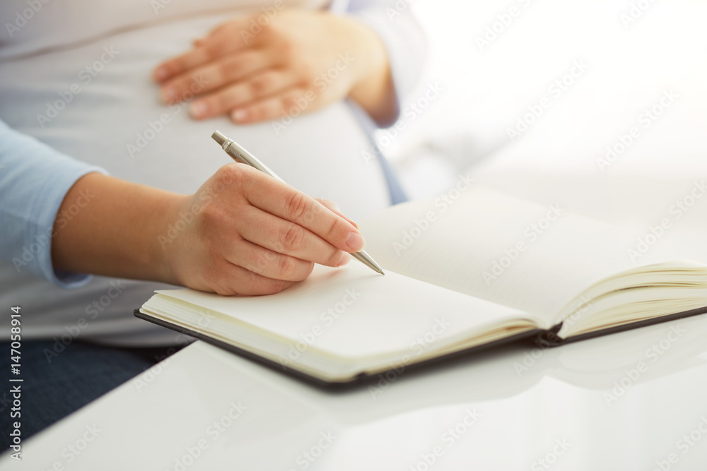 Young pregnant woman writes to her diary on a white table Young pregnant woman writes to her diary on a white table