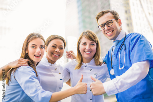 Four happy medical workers stand together and two of them show thumbs up  outdoors