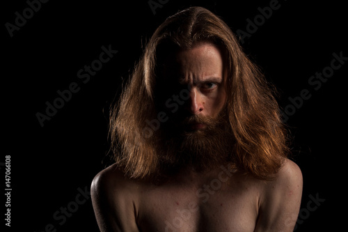 Hipster with long hair and beard on black backgroundin studio photo. Expression and fashion