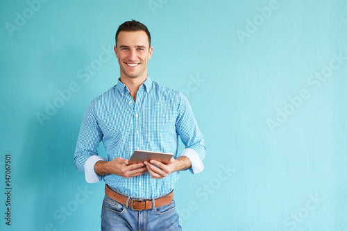 Smiling man with tablet computer standing in front of turquoise wall