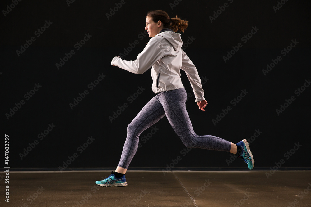 Young woman runner is seen running in an abandoned hall. Running is a good exercise for cardio vascular system and general health and weight control.
