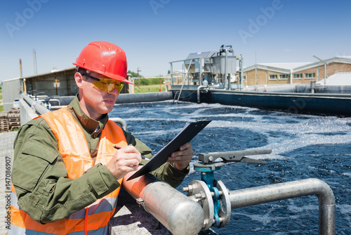 An engineer controlling a quality of water ,aerated activated sludge tank at a waste water treatment plant, writing facts photo