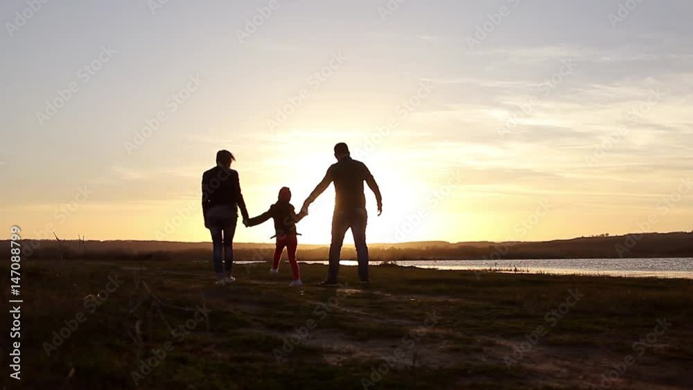 Silhouette, happy child with mother and father, family at sunset, summertime. Run, raising baby up in the air, hugs, love, playing. We are happy family.