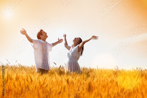 Happy, young couple with arms outstretched ,enjoying in the wheat field, summer season. Sunset light, flare light, copy space 
