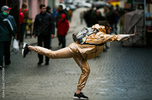 Woman in golden suit poses with raised hand and leg on the street