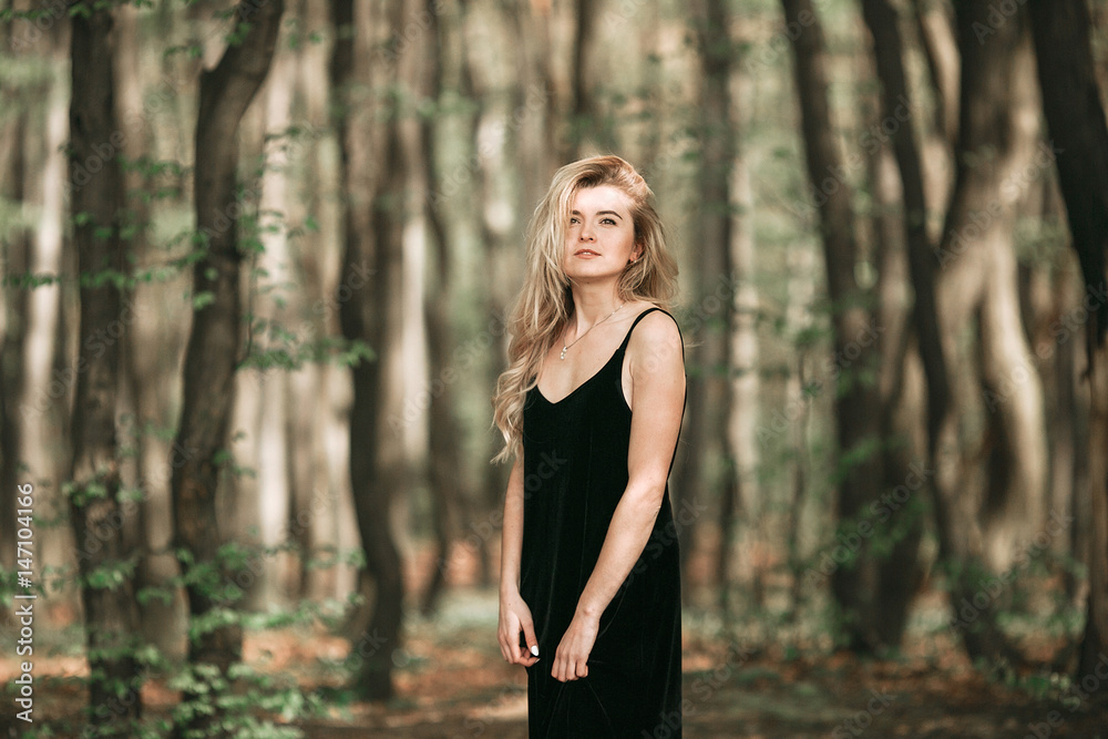 Girl in black velvet dress stands in the forest