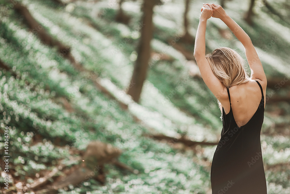 Blonde woman in black dress stretches in the forest