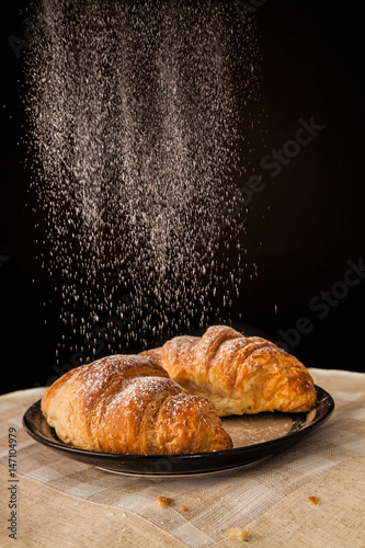 Photo Two fresh croissants being dusted with icing sugar