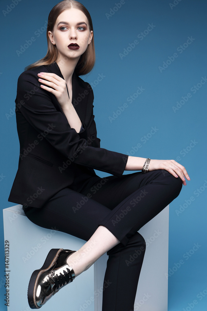 High fashion portrait of young elegant woman in black suit and loafers. High fashion portrait of young elegant woman in black suit and loafers.