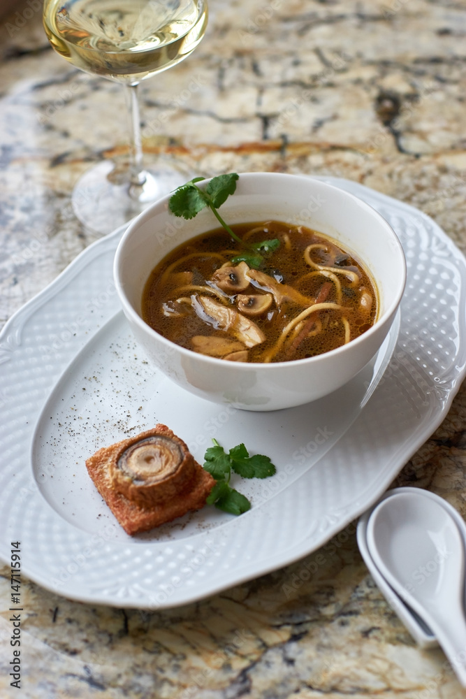 Asian cuisine. Mushroom soup with egg noodles served with toast, bread and white wine on marble background. Asian cuisine. Mushroom soup with egg noodles served with toast, bread and white wine on marble background.