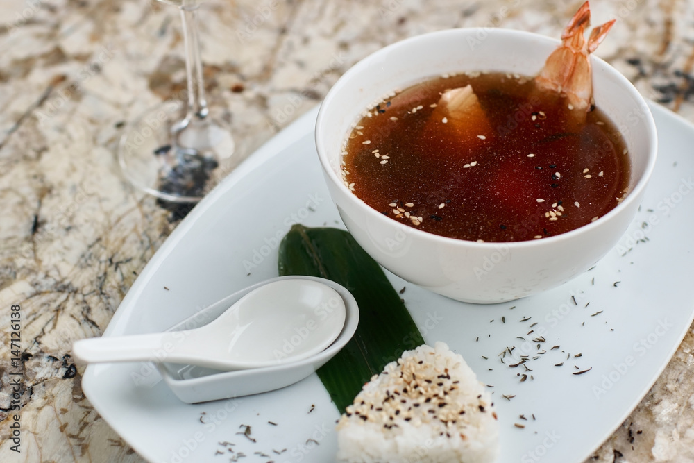 Japanese cuisine. Suimono or Matsutake soup served in white ceramic plate with spoon, rice and white wine on marble background. Japanese cuisine. Suimono or Matsutake soup served in white ceramic plate with spoon, rice and white wine on marble background.