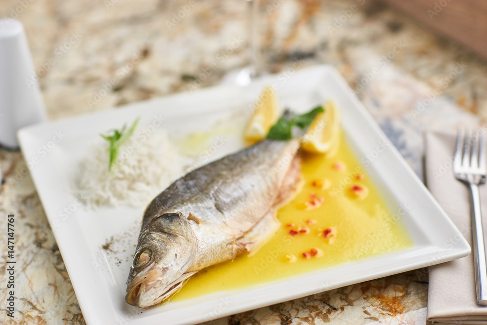 Whole boiled wolffish served with sauce from lemon butter and white wine on square white plate Whole boiled wolffish served with sauce from lemon butter and white wine on square white plate