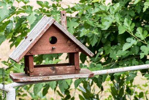 Brown wooden birdhouse with foliage blurred in background © Garry0305