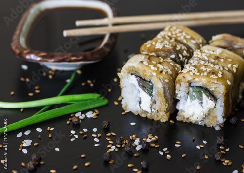 Japanese eel suhsi rolls with sesame seeds, avocado, chopsticks and soy sauce on black background  photo