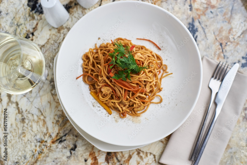 Flat egg noodles with vegetables served in big white ceramic round plate with glass of white wine on marble table Flat egg noodles with vegetables served in big white ceramic round plate with glass of white wine on marble table