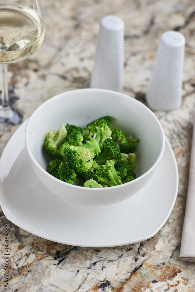Steamed broccoli served in white bowl with glass of white wine on marble background Steamed broccoli served in white bowl with glass of white wine on marble background