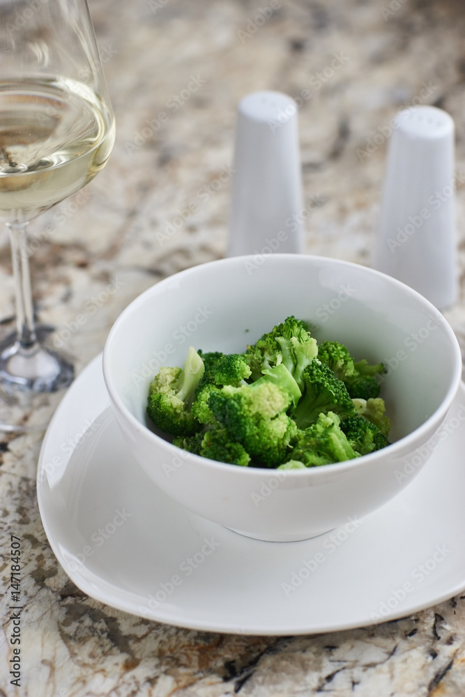 Steamed broccoli served in white bowl with glass of white wine on marble background Steamed broccoli served in white bowl with glass of white wine on marble background