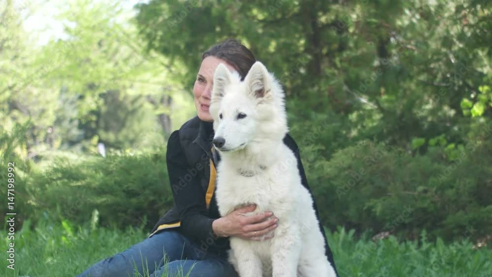 Cute girl and a puppy of a white Swiss sheepdog looking at a green lawn Cute girl and a puppy of a white Swiss sheepdog looking at a green lawn
