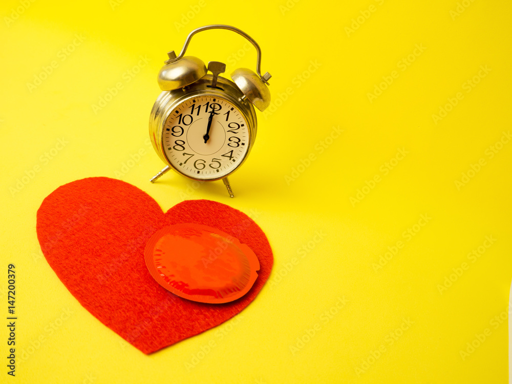 iron retro clock shows 12 hours. lying next to a red heart and a condom. the concept of safe sex iron retro clock shows 12 hours. lying next to a red heart and a condom. the concept of safe sex