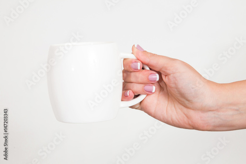 Closeup of beautiful female hand holding white mug isolated over white background. Fingernails with french pink manicure. Horizontal color photo.