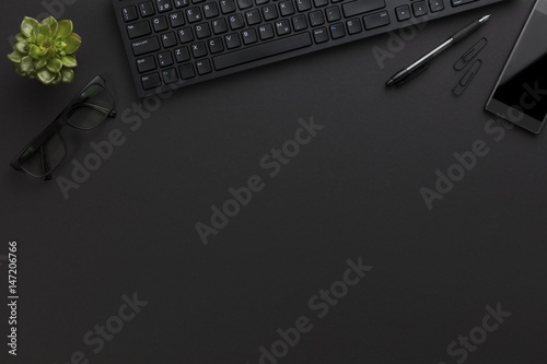 Top view of black office desk with computer and supplies