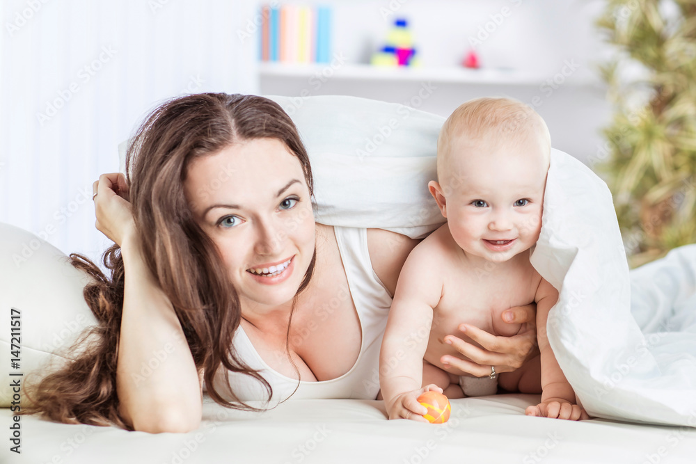 concept of happy mothers: happy mother and her year-old child playing on the sofa in the bedroom concept of happy mothers: happy mother and her year-old child playing on the sofa in the bedroom